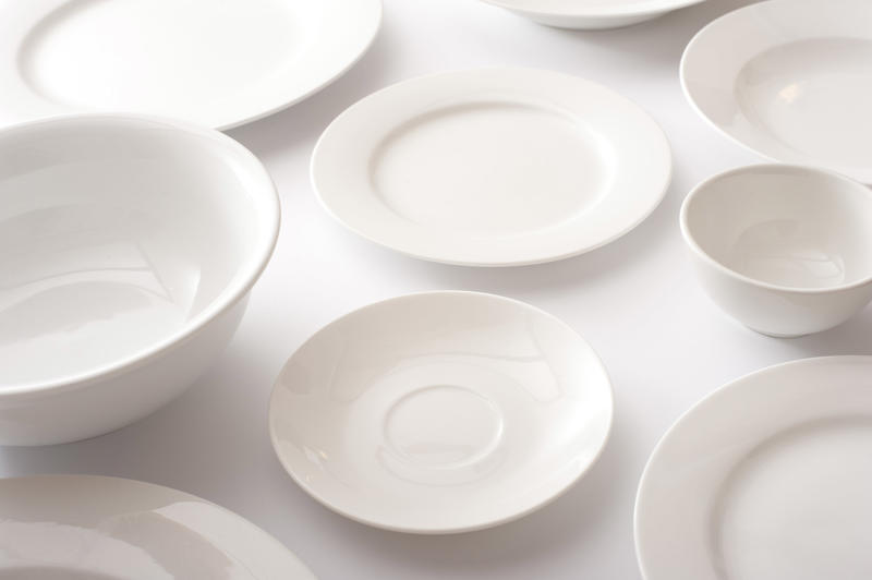 Assorted clean white plates, saucers and bowls laid out on a white table in a close up view