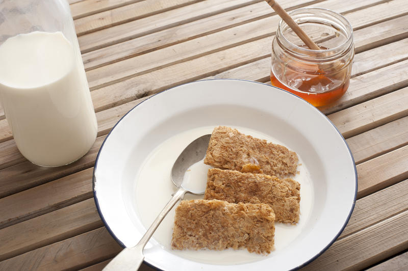 Wholewheat breakfast cereal served in a bowl with milk and honey on a slatted wooden table, high angle view