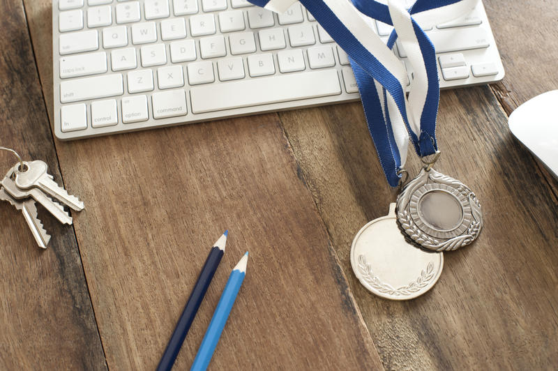 High Angle View of Rustic Wooden Computer Desk with Keyboard, Mouse, Colored Pencils, Keys and Silver Award Medals - Still Life with Copy Space