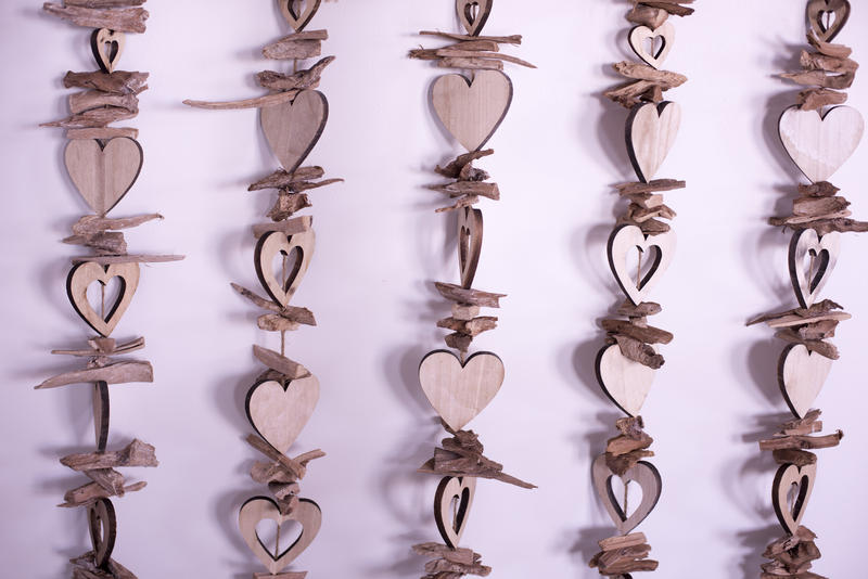 Wooden colourless heart shapes strung on strings, hanging close to pink background as vertical lines. Background concept