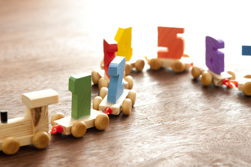 Colorful wooden kids numbers train with an engine pulling numerals on carriages to teach basic counting and arithmetic, with copy space