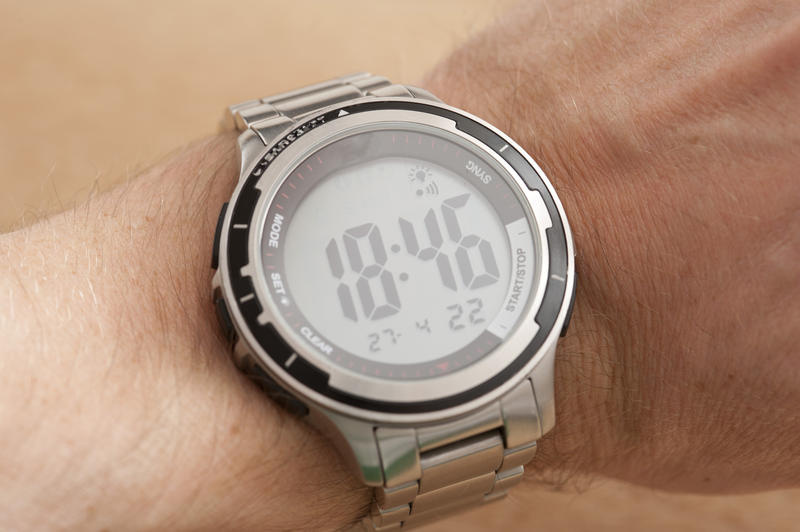 Sport silver electronic watch on the wrist of a man with round display showing an evening hour, close-up