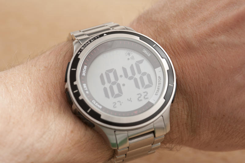 Sport silver electronic watch on the wrist of a man with round display showing an evening hour, close-up