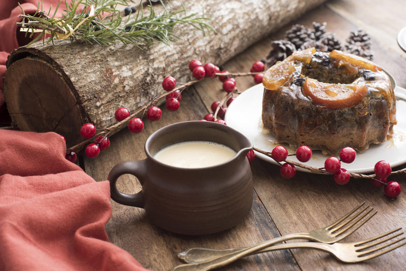 Homemade traditional Christmas pudding on a decorated Xmas table with a jug of brandy sauce alongside