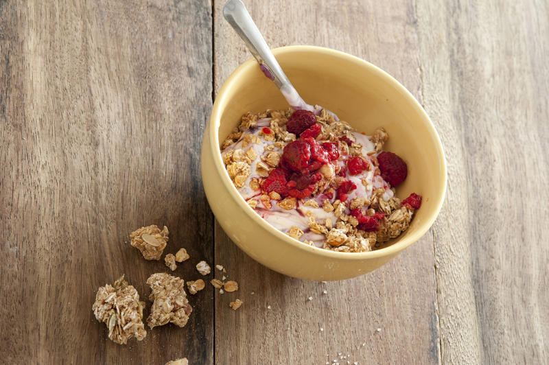 Overhead view of yellow bowl with muesli and raspberries with silver spoon on rustic wood table