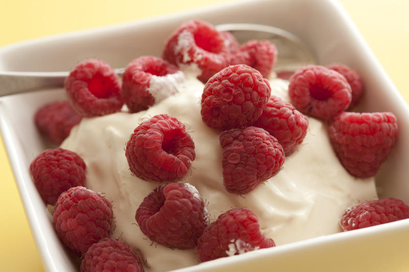 Plain creamy yogurt topped with fresh raspberries in a box shaped bowl with spoon