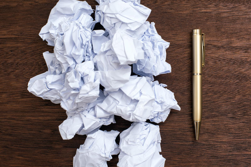 Writers block and bad ideas concept with a bunch of crumpled papers and a pen on viewed in close-up from above on wooden table surface