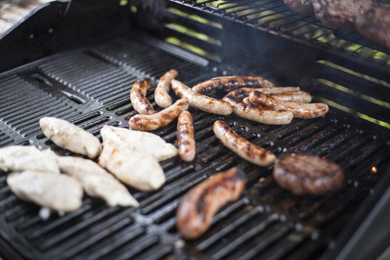 Assorted meats grilling on a barbecue fire with chicken, beef patties and sausages