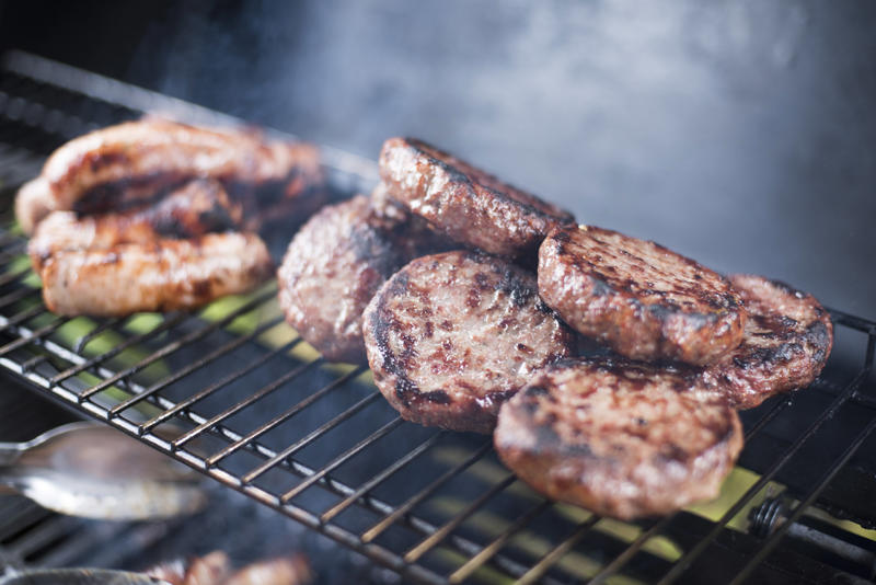 Beef burger patties and sausage on a BBQ grilling over the hot coals with smoke in a close up view