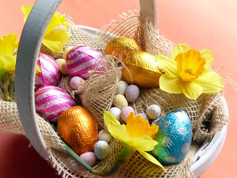 Basket of colorful chocolate easter eggs and quail egg candies, decorated with yellow daffodils and rustic sack cloth