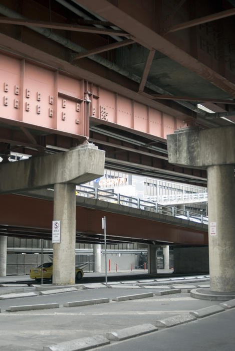 Urban road below flyover with yellow car passing by behind concrete support pillar