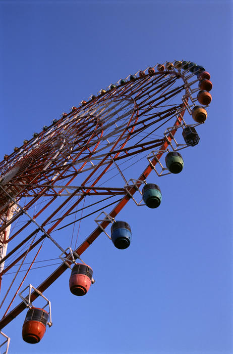 Colorful gondolas suspended from the rim on a big ferris wheel at an amusement park against a sunny blue sky