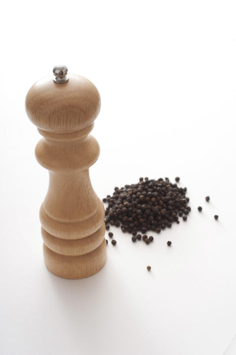 Heap of black peppercorns with a wooden pepper mill or grinder over a white background with copy space