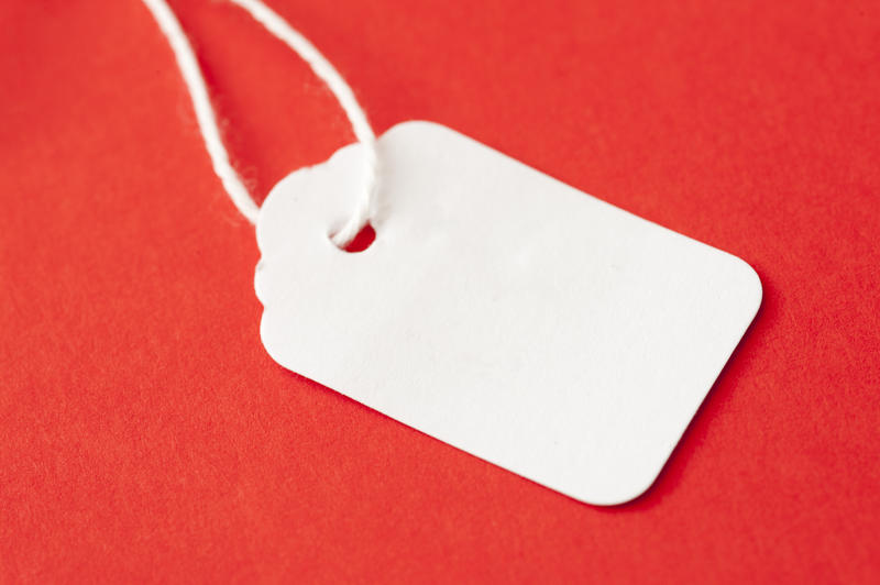 Blank white cardboard price ticket, tag or label on string lying on a festive red background