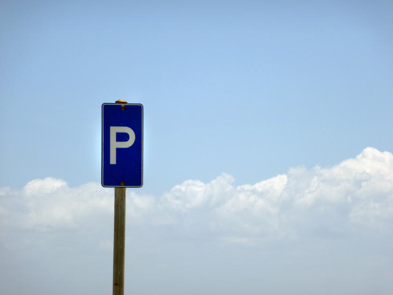 Blue parking sign on a tall pole in front of a cloudy sunny blue sky with copy space