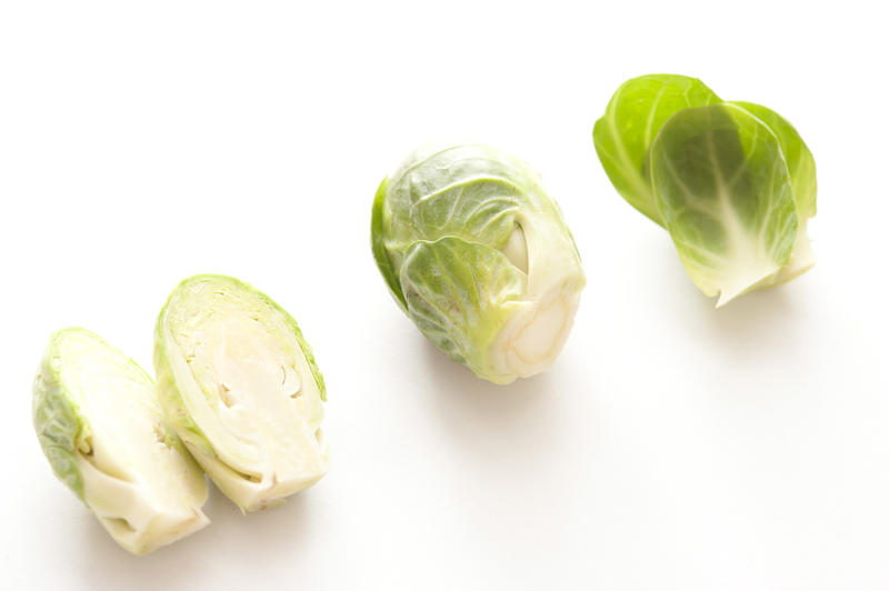 Heads of fresh green Brussels sprouts on white surface with shadow, cut in half and whole, viewed in close-up