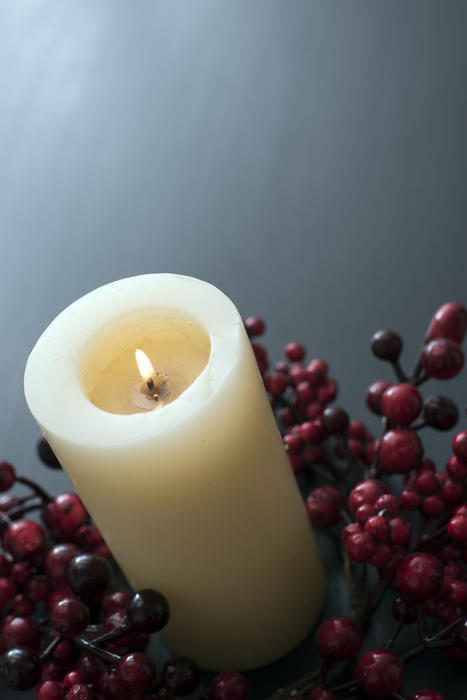 high angle view of a lit church candle, with a wreath of red berries and copyspace on a table behind