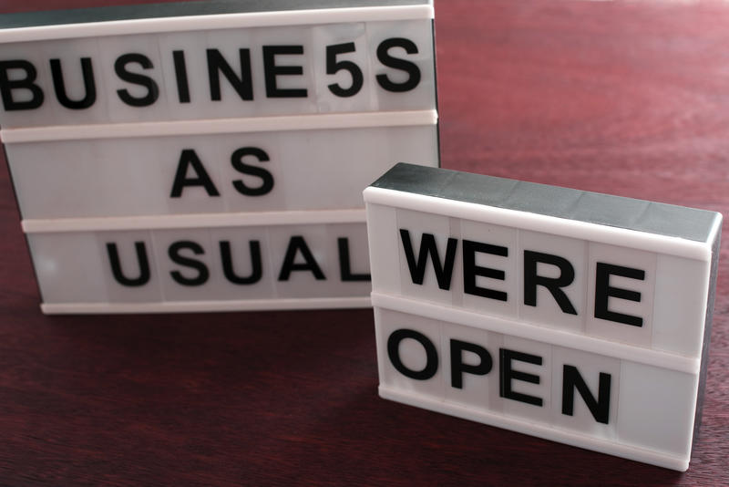 Two signs outside a business or store stating Business As Usual and Were Open viewed high angle