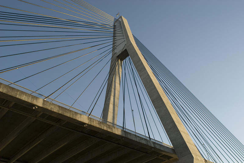 a low angle view of a concrete tower and support wires supporting the deck structure of a cable stayed bridge