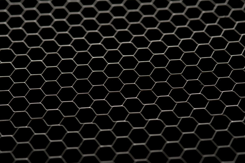 A close up of a chicken wire fence on a black background.