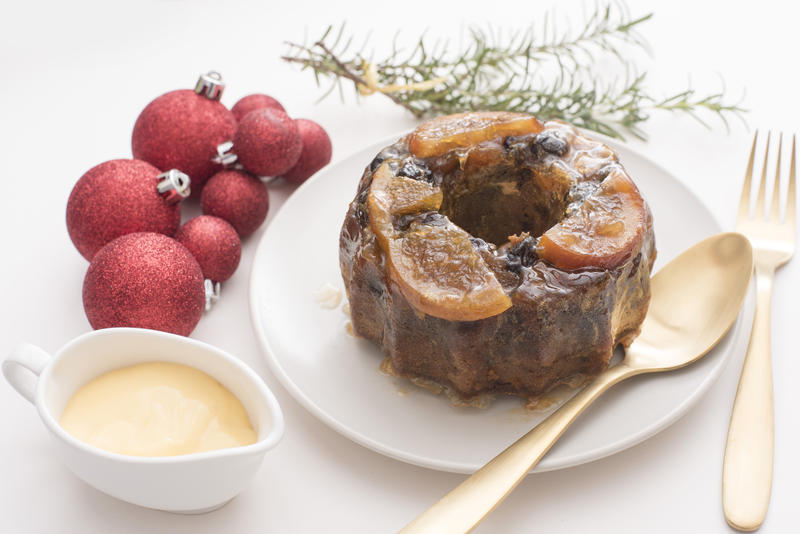 a christmas fruit pudding with brandy custard served on a plate with cutlery