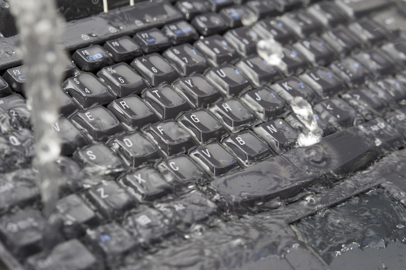 Cleaning up data concept pouring water on a black computer keyboard to flush it through in a close up full frame view