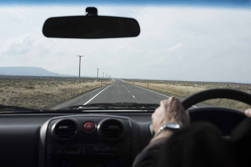 First person point of view of driving a car looking through the windscreen at the clear empty road ahead with hands on the steering wheel