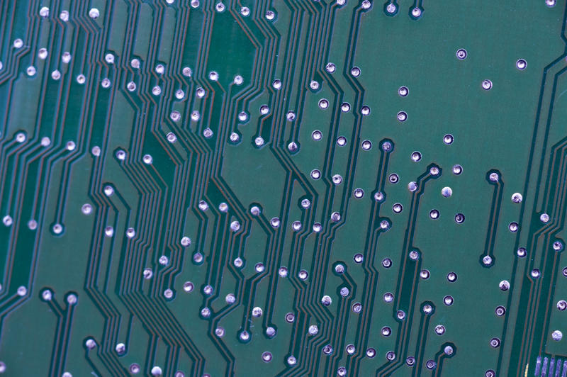 Full frame close-up of electronic circuit on green board with track connections an holes. Tech background concept