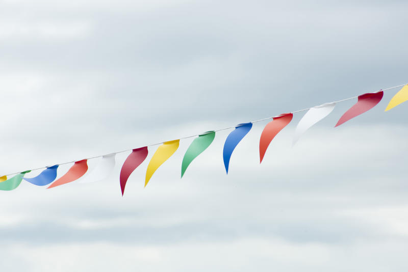 String of colourful triangular bunting flying against a cloudy grey sky conceptual of a festival, party or event