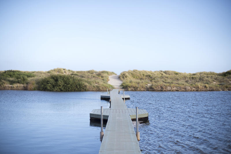 Floating pedestrian bridge crossing the lake or river with smooth and calm surface to the one side and ripples and waves to the other side of the pantones