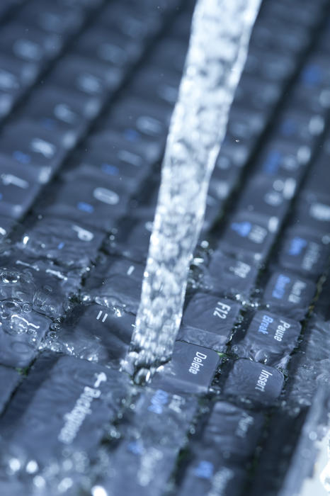 Data stream concept with running water onto computer keyboard, viewed in closeup