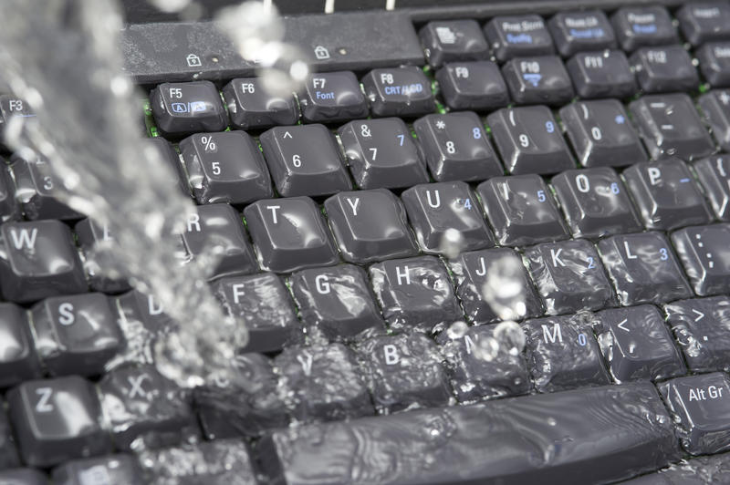 Concept of IT waste with water soaking a keyboard pouring from above in a steady stream in a close up full frame view