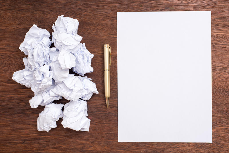 Concept of writers block or mental problem with crumpled paper alongside a blank white page with a pen on a wooden desk