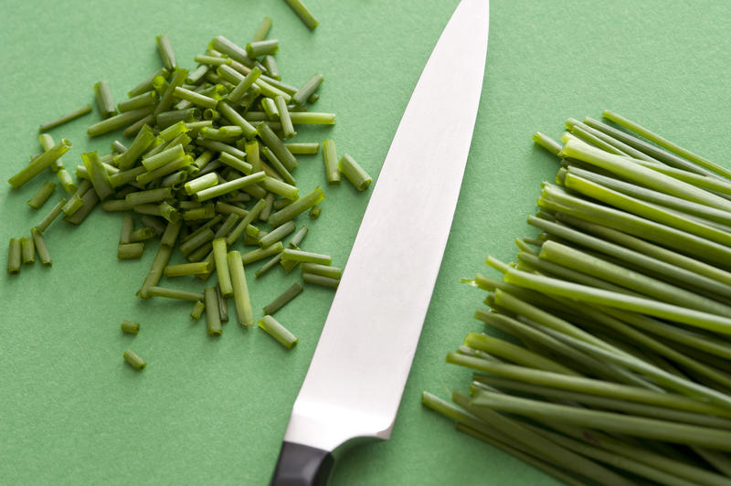 A close up of a sharp knife and chopped chives on a green background with copy space.