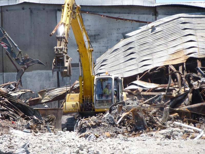 Demolition site with heavy duty machinery demolishing an old commercial building with piles of twisted metal debris