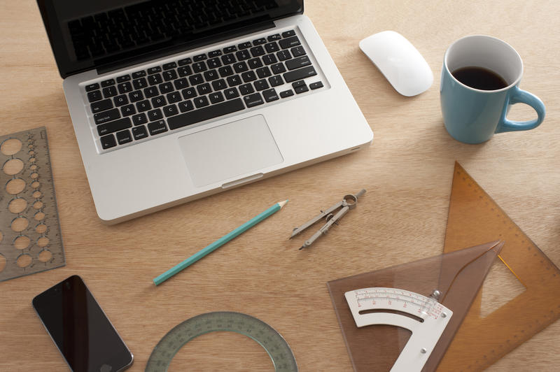 Workplace of an engineer or designer with rulers, electronic devices and a cup of coffee on the table, viewed in close-up from high angle