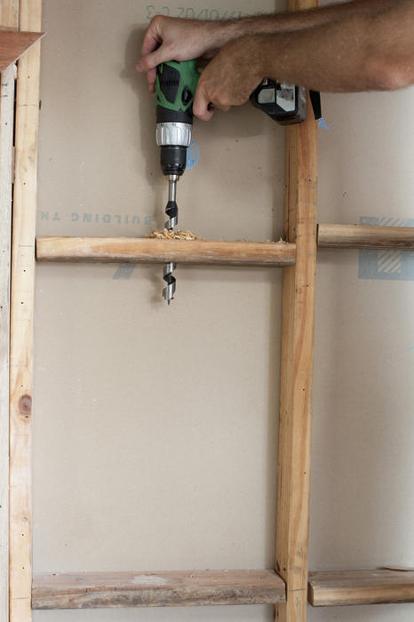 Builder drilling a hole in the wooden frame of a stud wall using a battery powered hand drill in a DIY or construction concept