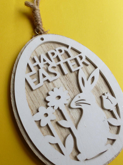 Happy Easter carved wooden pendant with rabbit and flowers, viewed in close-up on yellow background