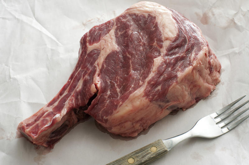 A close up of a raw eye steak and fork on butchers paper.