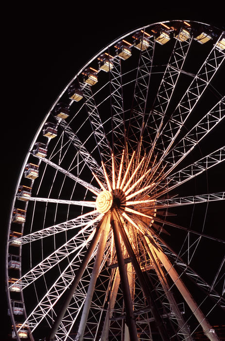 Illuminated ferris wheel at night on a fairground or amusement park against a dark sky in an entertainment concept