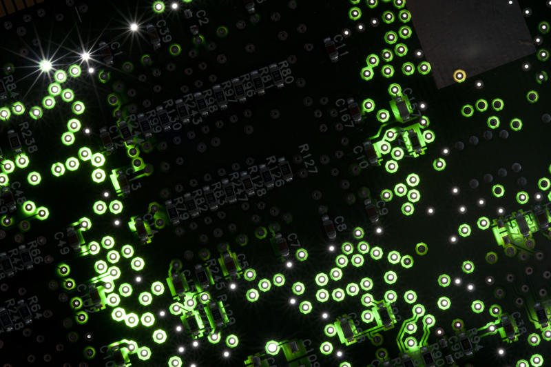 Glowing green electronic circuit on a printed circuit board with sparkling highlights in a full frame background