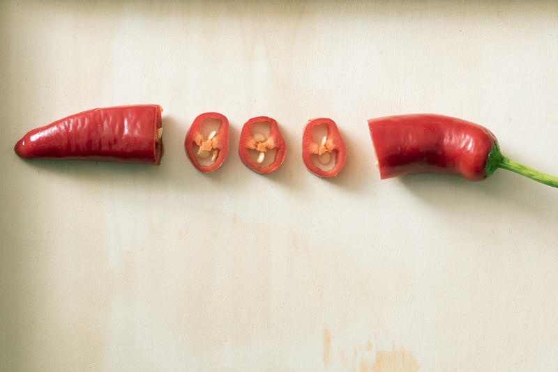 Diced red hot fresh chilli pepper pod showing the cross section between the tips over a textured white background with copy space