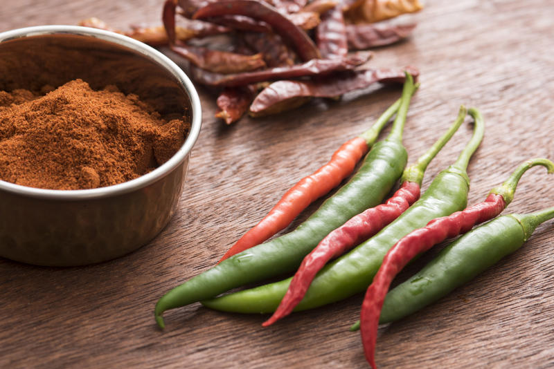 A bunch of fresh, dried and a bowl of powdered hot chilli pepper on kitchen table in close-up