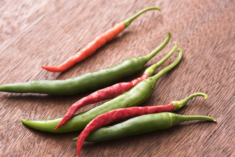 Red and green hot chilli peppers on brown wooden kitchen table in close-up