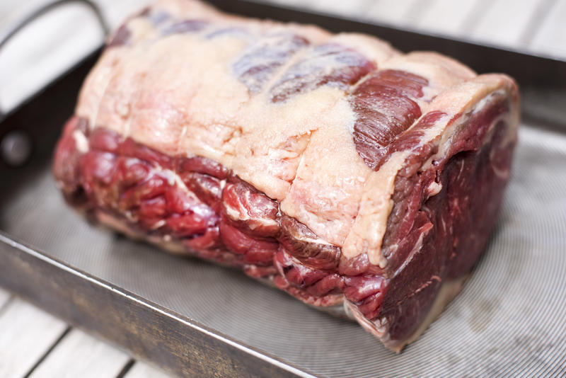 A close up of an uncooked, trussed joint of beef in an oven tray.