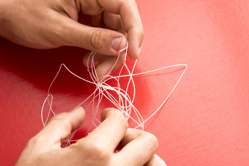 Solving problems concept with man untangling a knot in a piece of fine twine in a close up on his hands on a red background with copy space