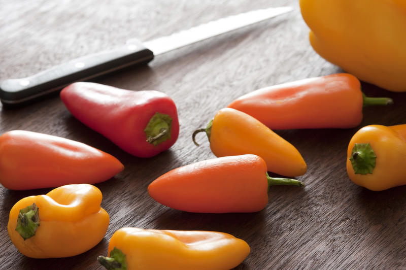 A close up of multicoloured mini capsicums and knife on a timber chopping block.