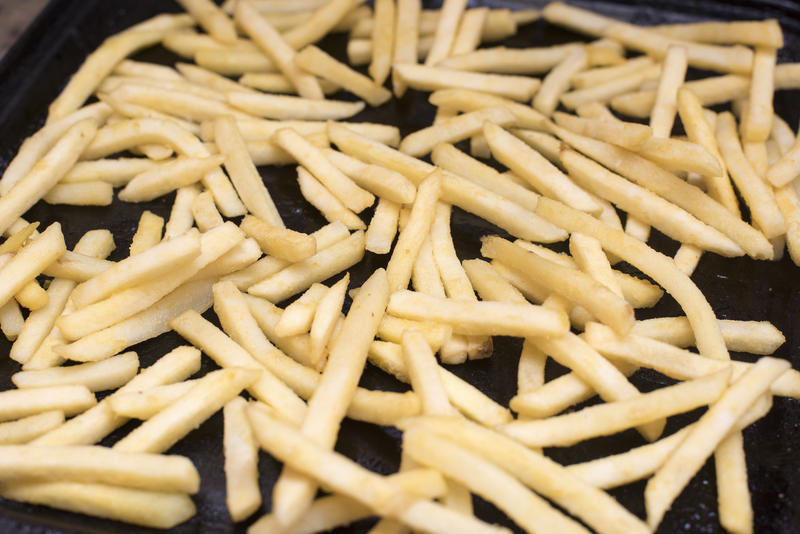 A close up of frozen potato chips in a black oven tray.