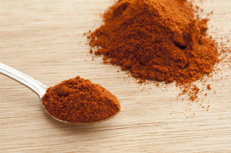 Spoonful of paprika with pile of ground spice alongside on a wooden table or chopping board