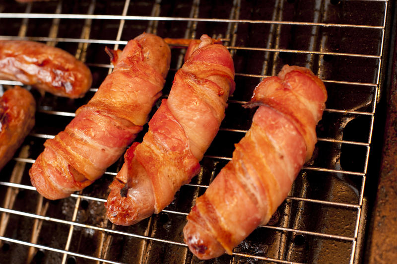 Grilled traditional pigs in blankets or pork sausages wrapped in rashers of bacon on a grill grid